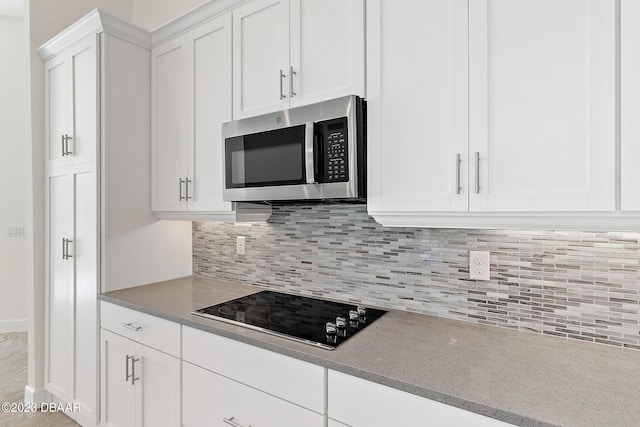 kitchen with black electric stovetop, tasteful backsplash, stainless steel microwave, white cabinetry, and light stone countertops