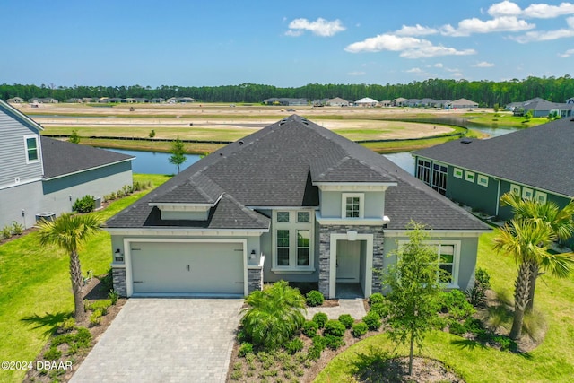 view of front facade featuring a garage, a shingled roof, a water view, stone siding, and decorative driveway