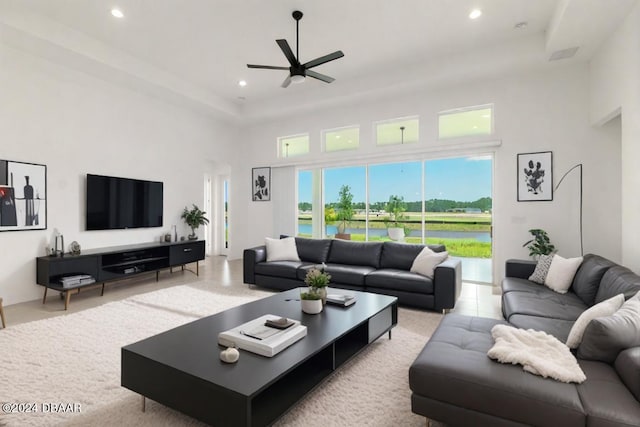 living room with ceiling fan, a high ceiling, a raised ceiling, and recessed lighting