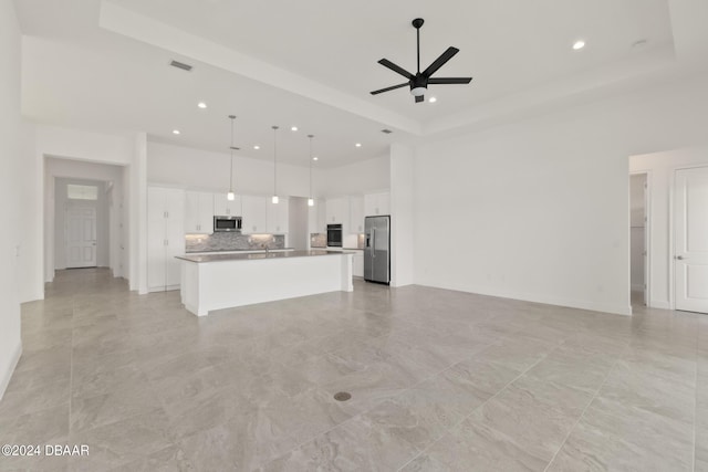 unfurnished living room featuring ceiling fan, a tray ceiling, and a high ceiling