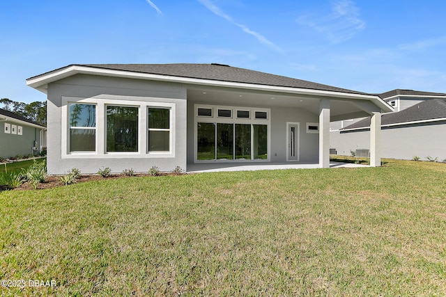 back of property with stucco siding, roof with shingles, a lawn, and a patio