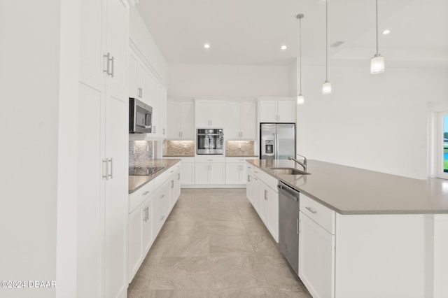 kitchen with stainless steel appliances, decorative backsplash, white cabinetry, a sink, and a large island with sink