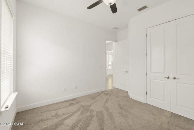 unfurnished bedroom with light carpet, a closet, and ceiling fan