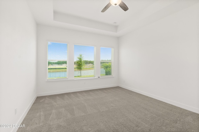 empty room featuring a raised ceiling, a water view, light colored carpet, and ceiling fan