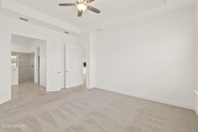 unfurnished bedroom with ceiling fan, a raised ceiling, and light carpet