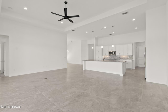 unfurnished living room with a raised ceiling, a towering ceiling, and ceiling fan