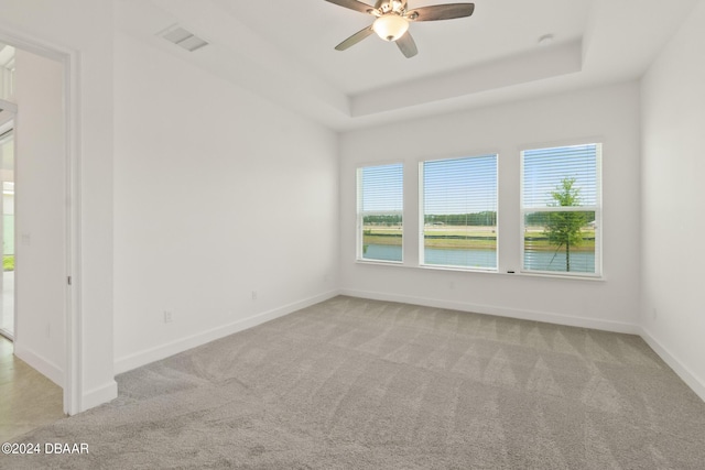 carpeted spare room featuring a raised ceiling, a water view, and ceiling fan