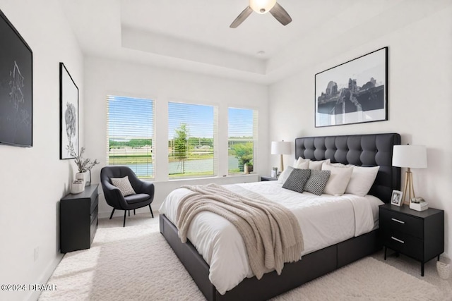 bedroom with a water view, ceiling fan, a tray ceiling, and light carpet