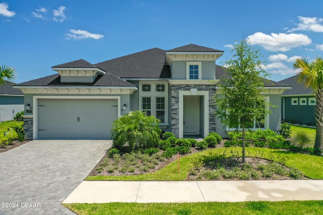 view of front facade featuring decorative driveway, stone siding, an attached garage, and stucco siding