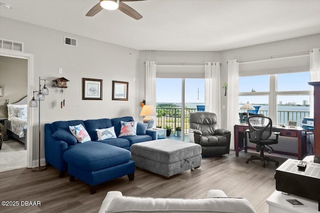 living room with a ceiling fan, visible vents, a water view, and wood finished floors