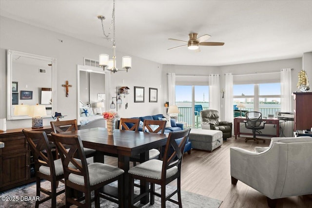dining space featuring wood finished floors, visible vents, a water view, and ceiling fan with notable chandelier