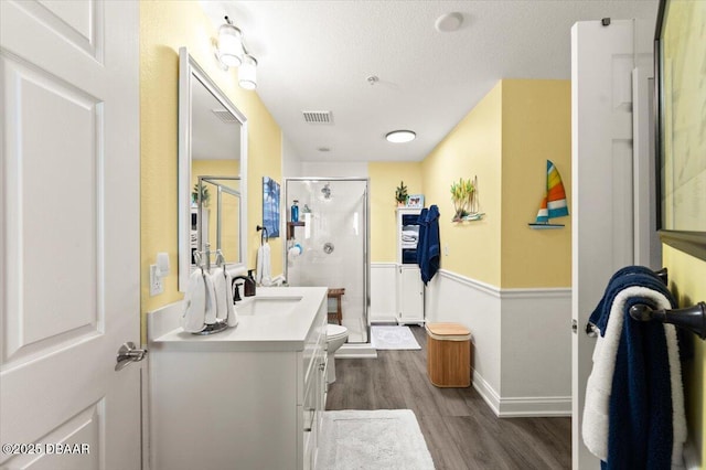 bathroom featuring a shower stall, vanity, toilet, visible vents, and wood finished floors