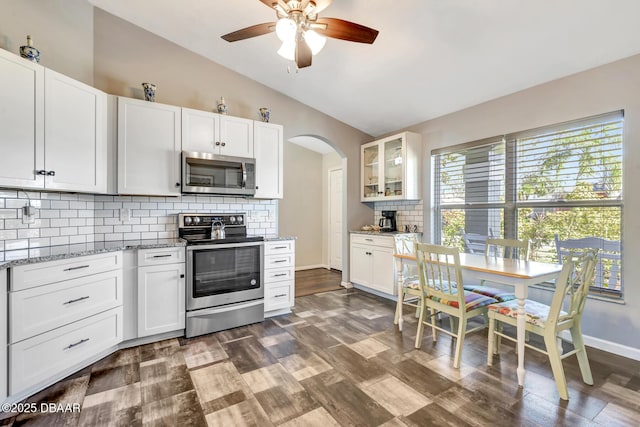 kitchen featuring tasteful backsplash, light stone counters, stainless steel appliances, vaulted ceiling, and white cabinetry