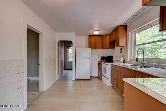 634 Aberdeen St, Daytona Beach, FL 32114 - kitchen with white appliances, light countertops, a sink, brown cabinetry, and arched walkways