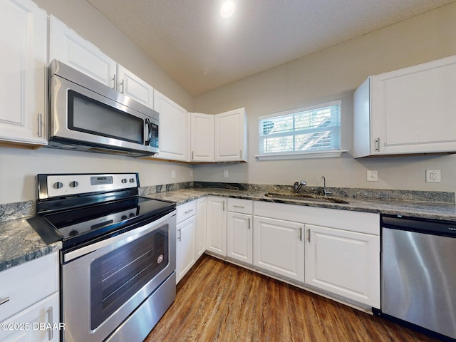 kitchen with white cabinetry, stainless steel appliances, dark wood-type flooring, dark stone counters, and sink