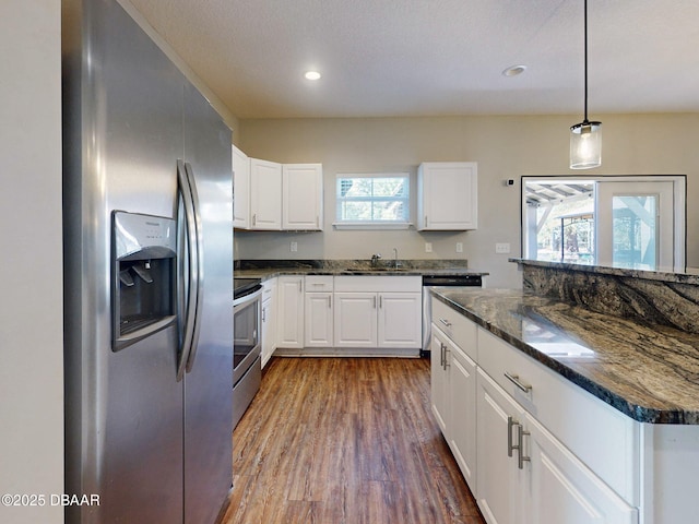 kitchen featuring white cabinets, decorative light fixtures, stainless steel appliances, dark stone counters, and sink