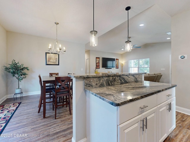 kitchen with vaulted ceiling, dark hardwood / wood-style floors, a kitchen island, white cabinetry, and dark stone counters