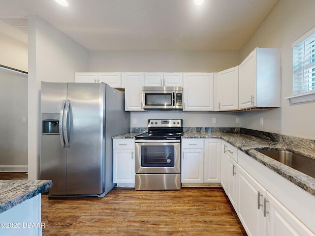 kitchen featuring appliances with stainless steel finishes, dark stone countertops, light hardwood / wood-style floors, and white cabinetry