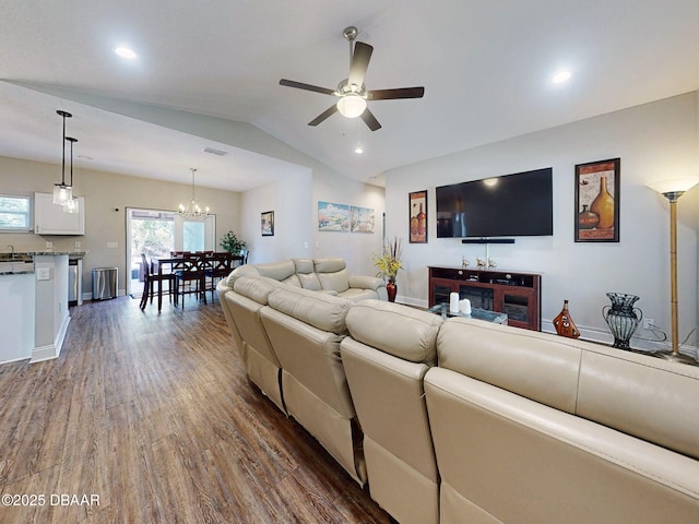 living room with ceiling fan with notable chandelier, dark hardwood / wood-style floors, and vaulted ceiling