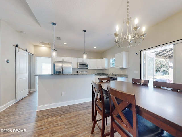 dining space with a barn door, sink, an inviting chandelier, and hardwood / wood-style flooring