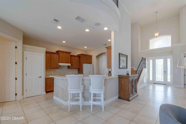 kitchen with a breakfast bar, light tile patterned floors, decorative light fixtures, a towering ceiling, and white refrigerator