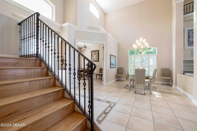 stairs featuring ceiling fan with notable chandelier, tile patterned flooring, and a towering ceiling