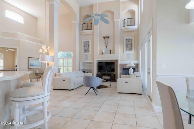 living room with a towering ceiling, ceiling fan with notable chandelier, light tile patterned floors, and decorative columns