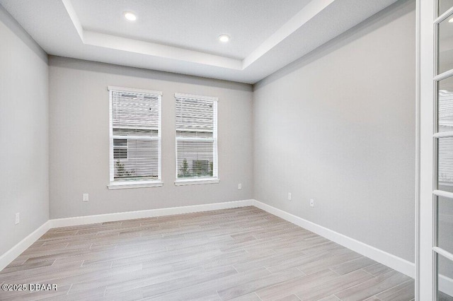 spare room with a raised ceiling and light hardwood / wood-style flooring