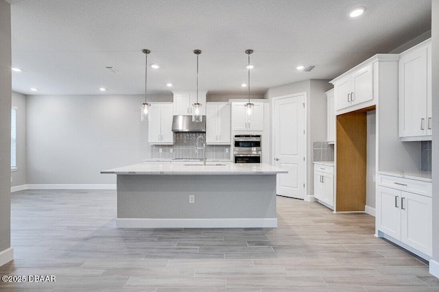 kitchen with sink, tasteful backsplash, an island with sink, white cabinets, and decorative light fixtures