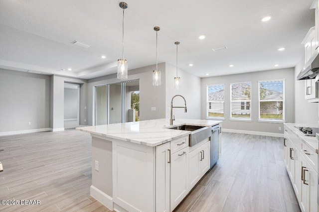 kitchen with decorative light fixtures, white cabinetry, dishwasher, sink, and a center island with sink