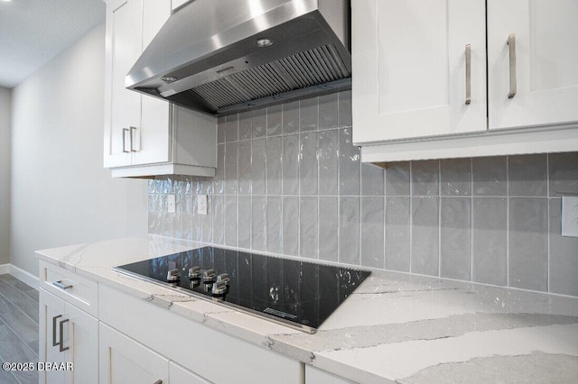 kitchen featuring wall chimney range hood, backsplash, light stone counters, black electric stovetop, and white cabinets