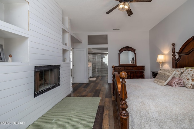 bedroom featuring dark wood-style flooring, a glass covered fireplace, ensuite bath, and visible vents