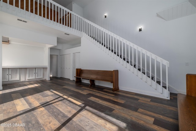 unfurnished living room featuring baseboards, visible vents, wood finished floors, stairway, and a high ceiling