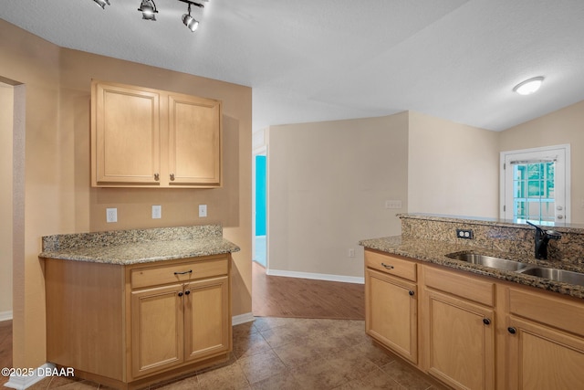 kitchen featuring lofted ceiling, light brown cabinets, a sink, light stone countertops, and baseboards