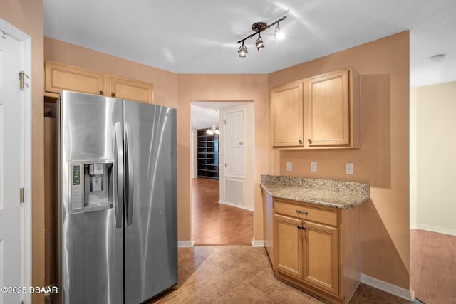 kitchen featuring baseboards, light brown cabinetry, light stone countertops, and stainless steel fridge with ice dispenser