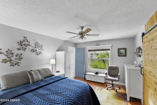 bedroom featuring hardwood / wood-style flooring, a textured ceiling, a barn door, and ceiling fan