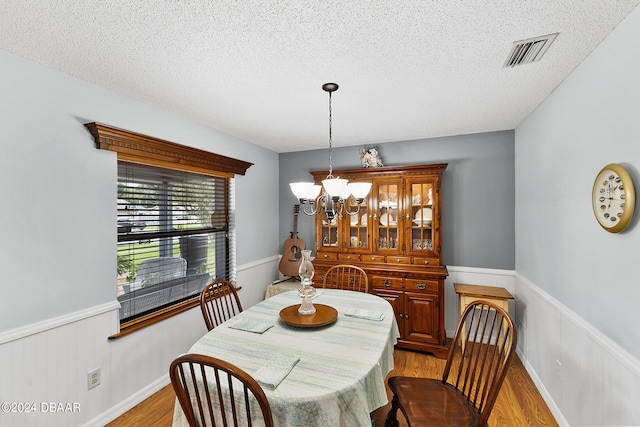 dining area with a textured ceiling, light wood-type flooring, and a chandelier