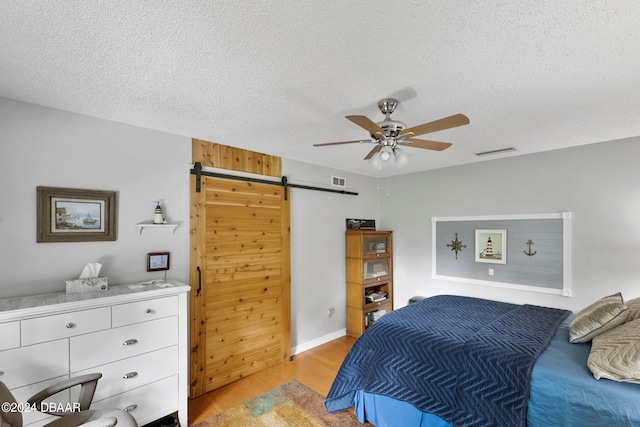 bedroom featuring a textured ceiling, light wood-type flooring, a barn door, and ceiling fan