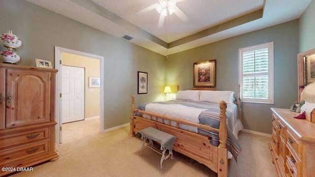 bedroom with light carpet, ceiling fan, and a raised ceiling