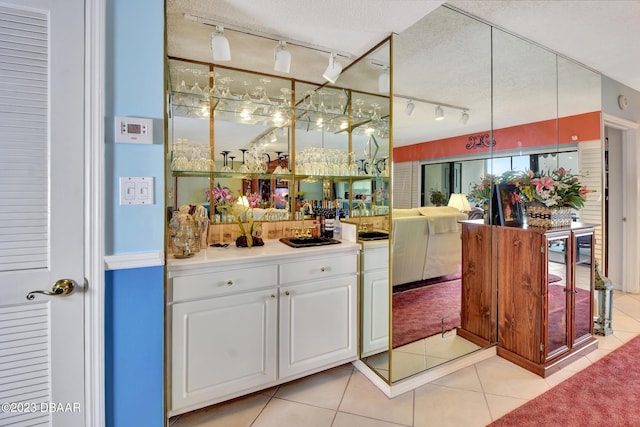 interior space with white cabinetry, a textured ceiling, rail lighting, and light tile patterned flooring