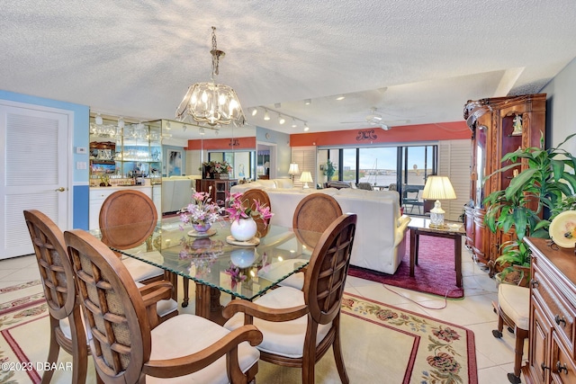 dining area featuring light tile patterned flooring, ceiling fan with notable chandelier, and a textured ceiling