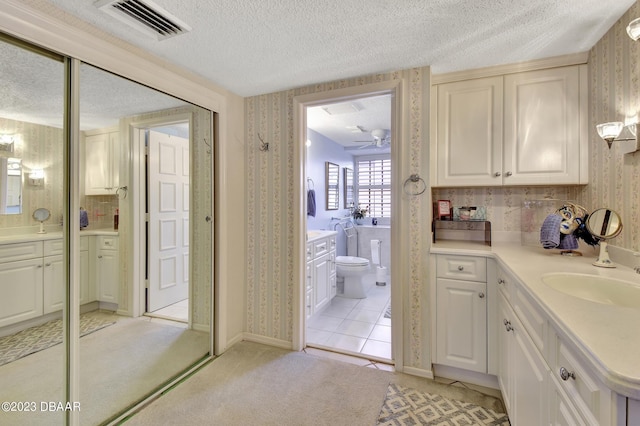 bathroom with toilet, tile patterned flooring, a textured ceiling, vanity, and ceiling fan