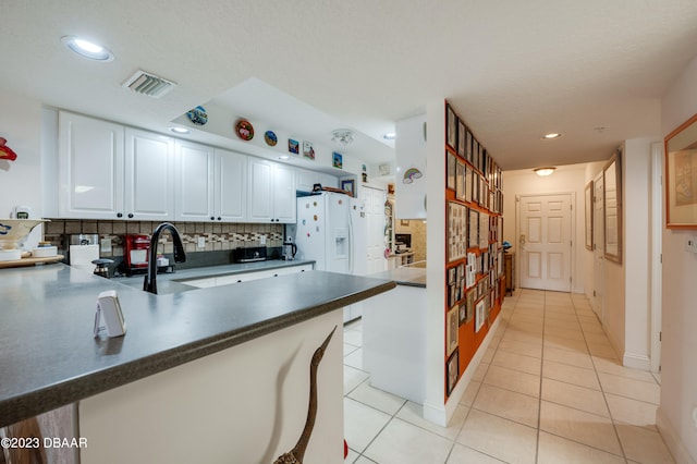 kitchen featuring light tile patterned flooring, a textured ceiling, decorative backsplash, white cabinets, and kitchen peninsula