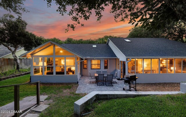 4791 S Peninsula Dr, Ponce Inlet, FL 32127 - back of house at dusk with fence, a shingled roof, a lawn, and a patio area