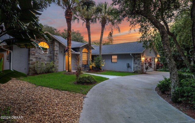 4791 S Peninsula Dr, Ponce Inlet, FL 32127 - view of front of home with driveway, stone siding, stucco siding, a shingled roof, and a yard