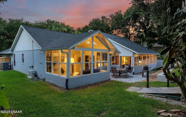 4791 S Peninsula Dr, Ponce Inlet, FL 32127 - back of property at dusk featuring a patio area, a sunroom, central AC, a yard, and a shingled roof