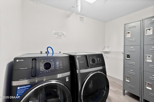 laundry area with separate washer and dryer, light hardwood / wood-style flooring, and a textured ceiling