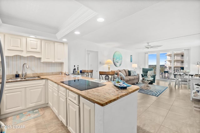 kitchen featuring sink, crown molding, black electric cooktop, a tray ceiling, and kitchen peninsula