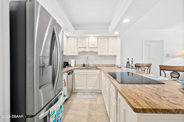 kitchen with sink, stainless steel appliances, ornamental molding, a raised ceiling, and kitchen peninsula