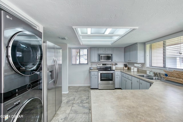 kitchen featuring a wealth of natural light, sink, stacked washer / drying machine, and appliances with stainless steel finishes